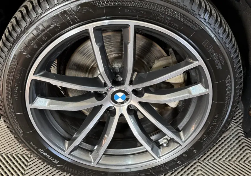 Gros plan sur la jante alliage grise et noire avec logo BMW au centre, montée sur pneu Kleber.