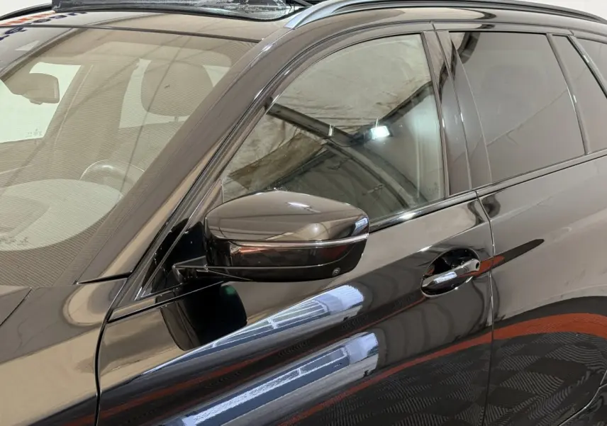 Gros plan sur la porte avant gauche noire d'une BMW Série 5 Touring 520d M Sport avec rétroviseur et poignée chromés.