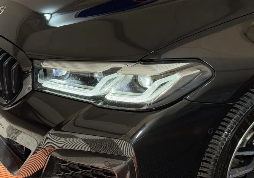 Gros plan sur le phare avant droit et la calandre noire brillante d'une BMW Série 5 Touring 520d M Sport 2023.