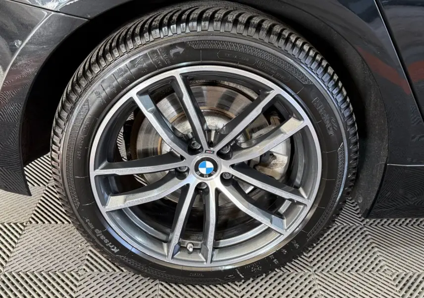 Gros plan sur la roue avant droite noire d'une BMW Série 5 Touring 520d M Sport avec jante alliage gris foncé.