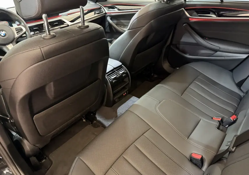 Vue intérieure arrière côté droit de la BMW Série 5 Touring 520d M Sport 2023 avec sièges cuir noirs et finitions rouges.