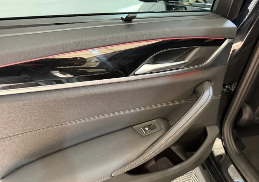Détail de la porte intérieure côté gauche d'une BMW Série 5 Touring noire avec insert brillant et éclairage d'ambiance rouge.