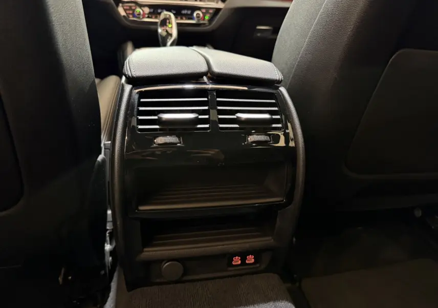 Vue rapprochée de la console centrale arrière noire avec aérateurs et commandes de chauffage sur BMW Série 5 Touring 520d 2023.