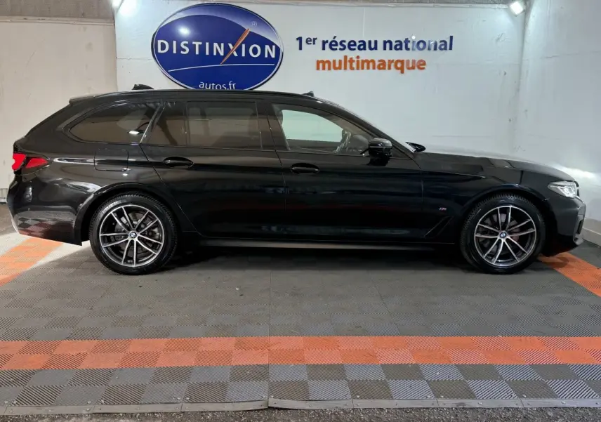 BMW Série 5 Touring 520d M Sport noir vue de profil côté gauche dans un garage avec sol gris et orange.