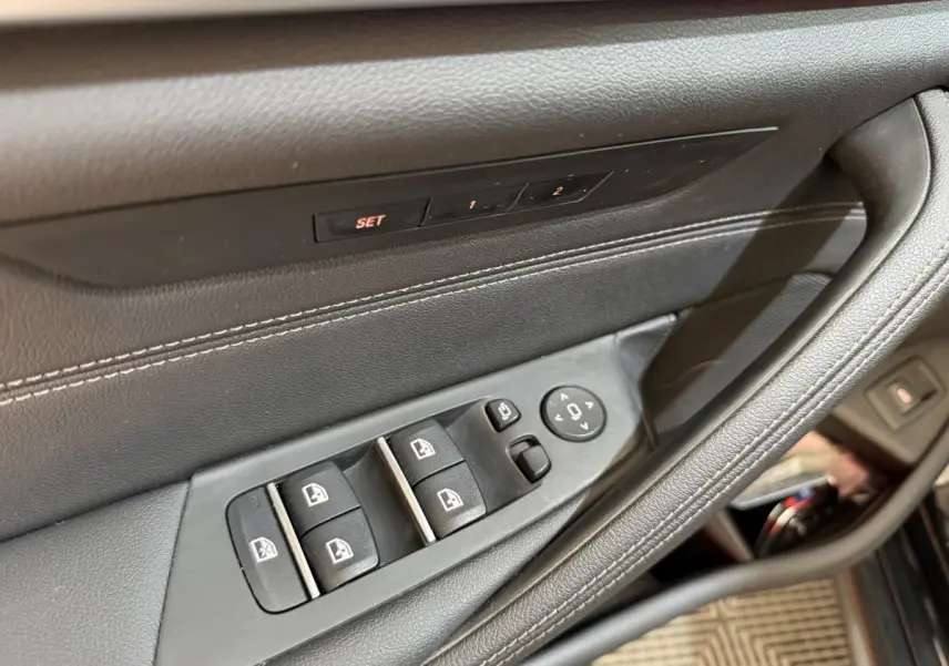 Gros plan sur la commande des vitres et réglages des rétroviseurs côté conducteur d’une BMW Série 5 Touring noire.
