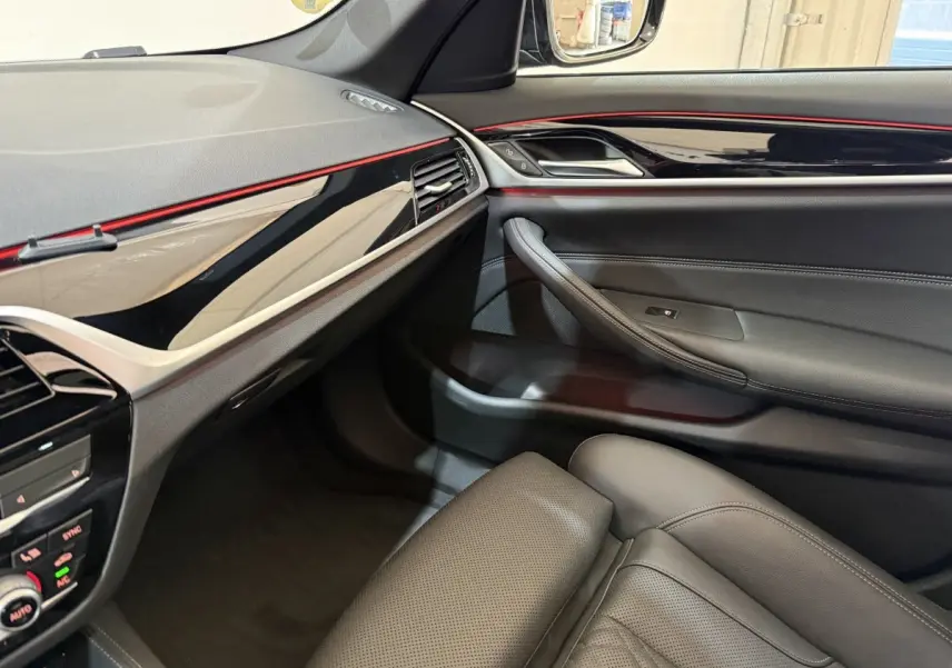 Vue intérieure côté passager de la BMW Série 5 Touring 520d M Sport 2023 avec garnitures noires et bandeau décoratif rouge.
