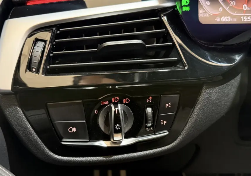 Gros plan sur la commande des phares et la sortie d'air noire du tableau de bord d'une BMW Série 5 Touring 520d 2023.