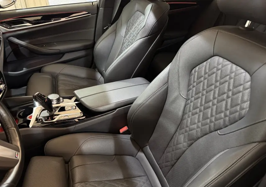 Vue intérieure côté conducteur et passager avant de la BMW Série 5 Touring 520d M Sport, sièges cuir noirs avec surpiqûres.