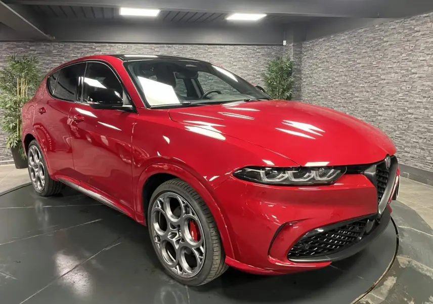 Alfa Romeo Tonale rouge 3/4 avant droit, jantes 20 pouces, rétroviseurs noirs et toit noir en intérieur showroom.