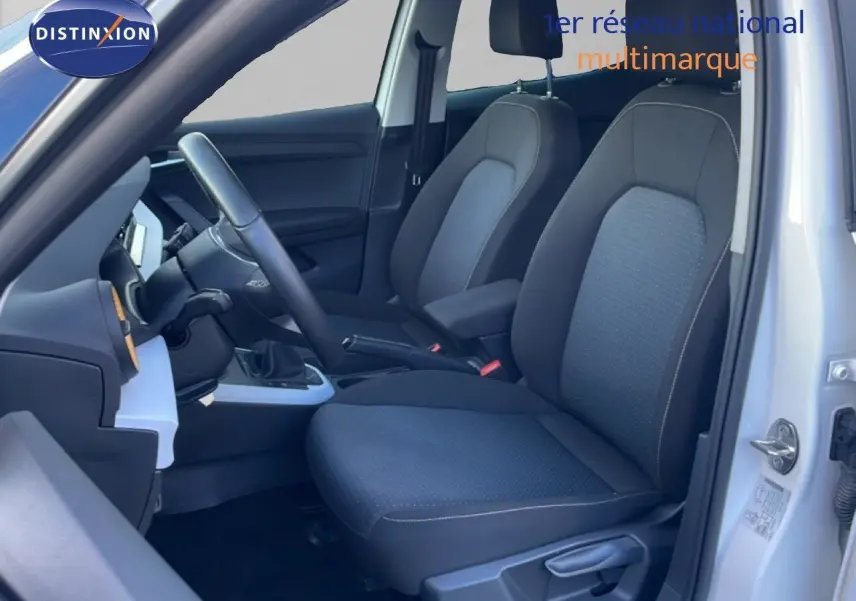 Vue intérieure côté conducteur du SEAT Arona 2025, sièges tissu gris foncé avec volant cuir et tableau de bord noir.