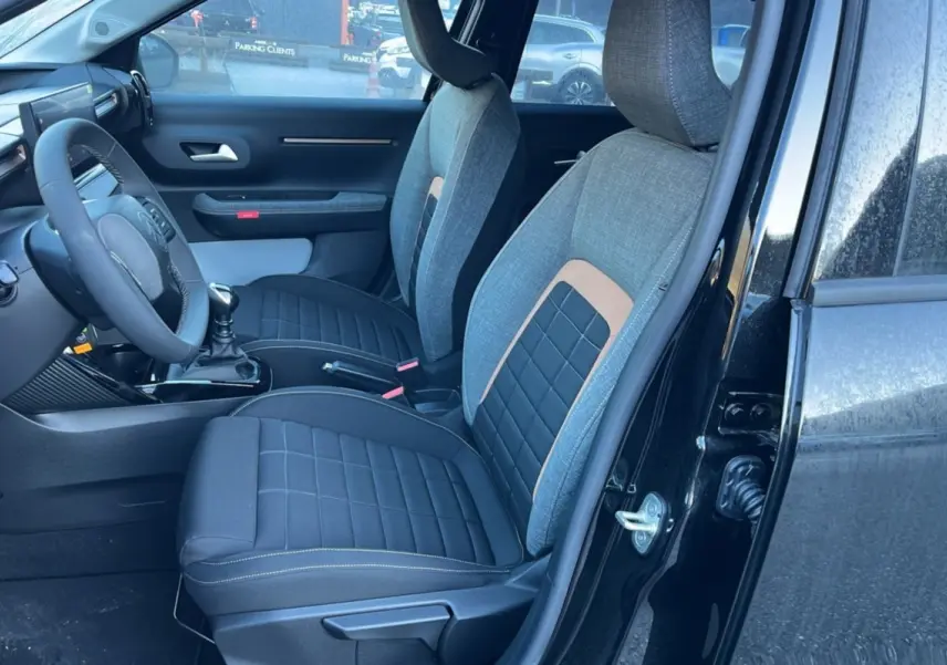 Vue intérieure côté conducteur de la Citroën C3 Aircross 2025 noir perla nera, sièges tissu bicolores et volant cuir multifonctions.