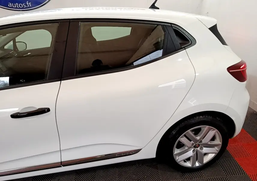 Vue latérale côté gauche d'une Renault Clio blanche avec jantes alliage et poignées de porte noires.