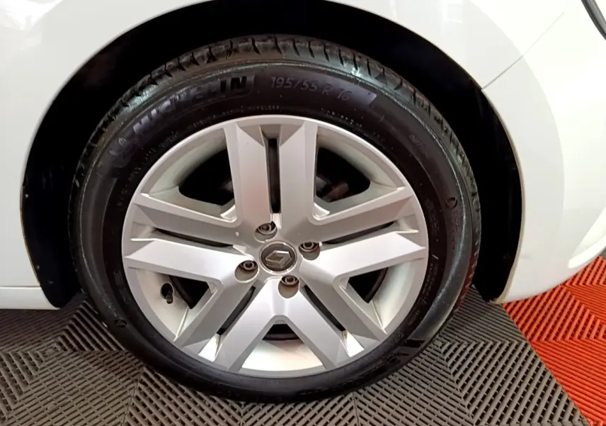 Vue rapprochée de la roue arrière droite d'une Renault Clio Business blanche, sur sol à motifs gris et rouge.