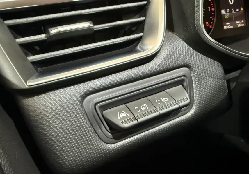 Gros plan sur les commandes d'assistance et réglage des phares à gauche du tableau de bord d'une Renault Clio Business blanche.