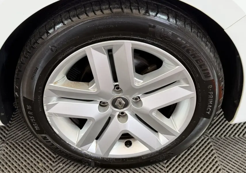 Gros plan sur la roue avant droite d’une Renault Clio blanche, jante alliage argentée à cinq branches doubles.