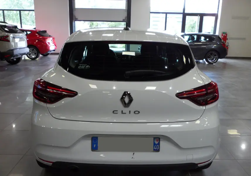 Vue arrière d'une Renault Clio V blanche Glacier en intérieur, avec feux arrière LED et logo central visible.