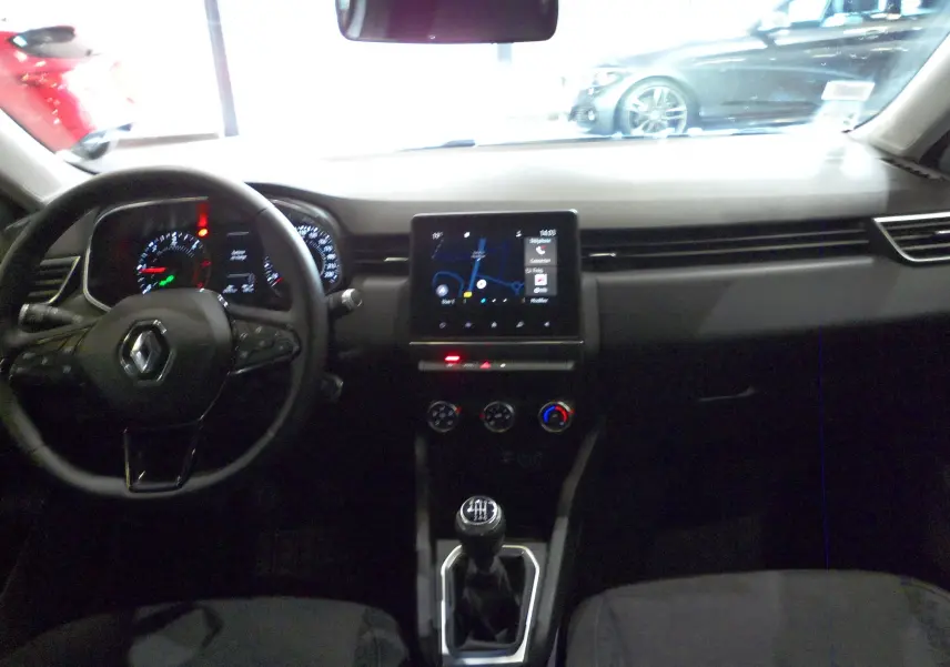 Vue intérieure avant de la Renault Clio V blanche, tableau de bord avec écran tactile et levier de vitesses manuel visible.