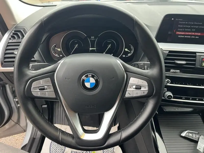 Vue intérieure centrée sur le volant cuir multifonction d’une BMW X3 xDrive30eA 2020, avec tableau de bord et écran tactile visibles.