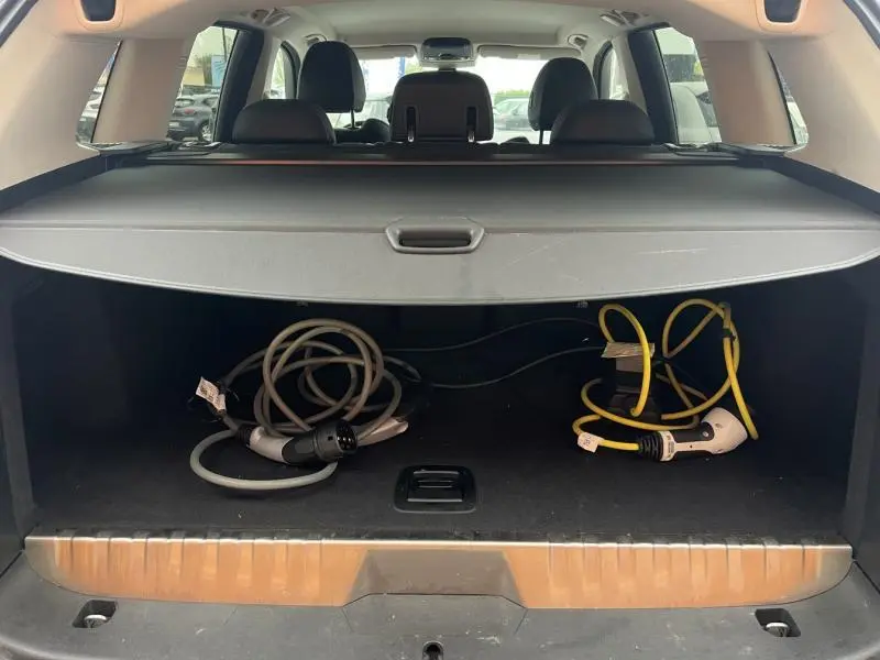 Coffre ouvert d’un BMW X3 xDrive30eA 2020 Glacier Silver, montrant câbles de recharge hybride et cache-bagages.