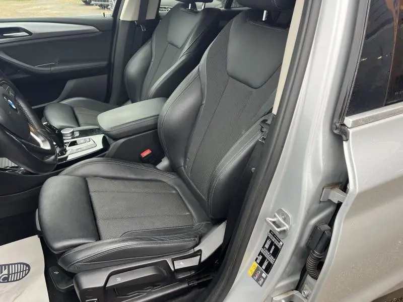 Vue intérieure côté conducteur d'une BMW X3 xDrive30e 2020 en Glacier Silver avec sièges avant en cuir noir et accoudoir central.