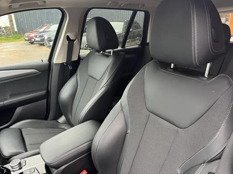 Vue intérieure rapprochée des sièges avant noirs en tissu et cuir du BMW X3 xDrive30eA 2020, avec accoudoir central.