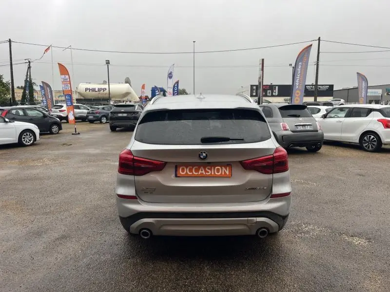 Vue arrière d'un BMW X3 xDrive30eA 2020 Glacier Silver avec double sortie d'échappement, en extérieur sur parking.