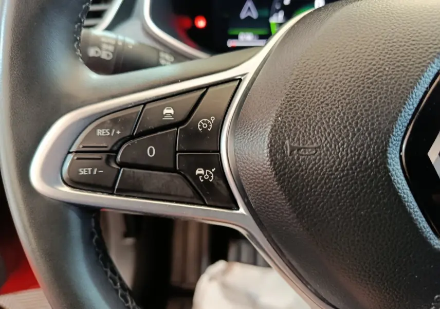 Gros plan sur les commandes de régulateur de vitesse à gauche du volant de la Renault Clio Techno TCe 90 rouge 2024.