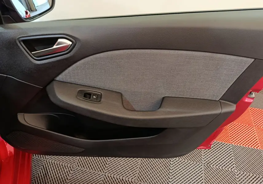 Vue rapprochée de la porte avant gauche rouge de la Renault Clio 2024, avec panneau intérieur noir et gris et commande de vitre électrique.