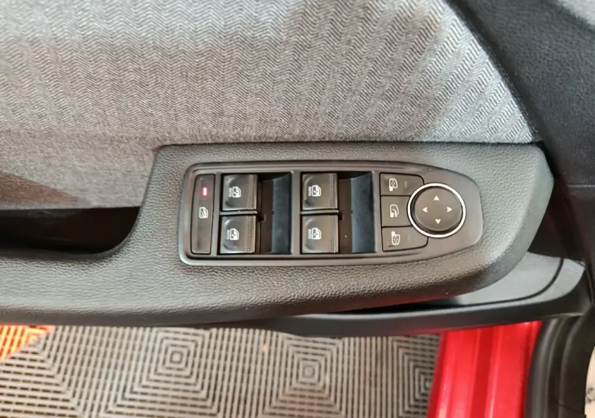 Vue rapprochée des commandes des vitres et rétroviseurs sur la porte côté conducteur d'une Renault Clio rouge 2024.