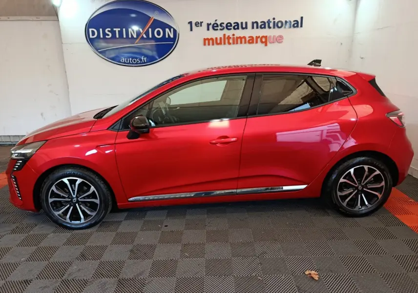 Profil côté gauche d'une Renault Clio Techno TCe 90 rouge 2024, avec jantes alliage et vitres teintées, en intérieur showroom.