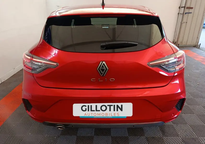 Vue arrière d'une Renault Clio rouge 2024 dans un garage, avec feux LED et logo Renault bien visibles.