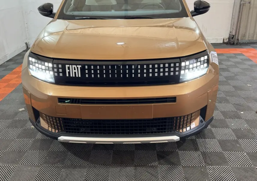 Vue frontale d'une FIAT Grande Panda marron 2025 avec calandre à damiers lumineux et phares LED allumés.