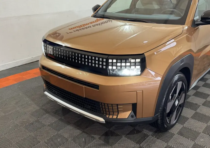 Vue 3/4 avant droite de la FIAT Grande Panda marron 2025 avec phares LED et calandre pixelisée distinctive.