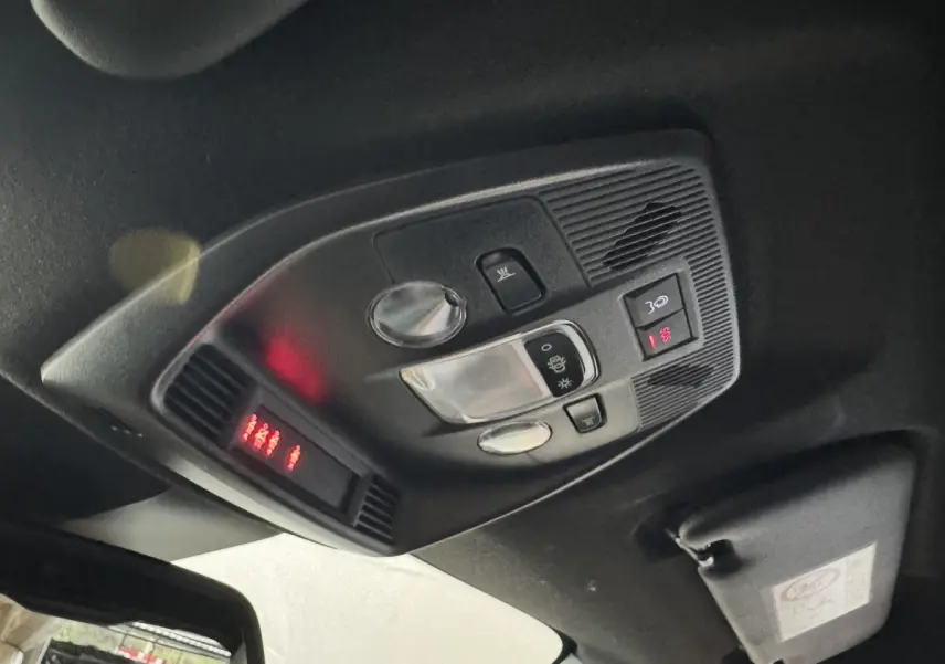 Vue intérieure en plongée du plafonnier noir avec commandes d’éclairage et affichage rouge de la FIAT Grande Panda marron.