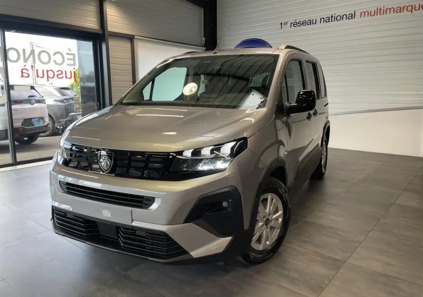 Peugeot Rifter gris Artense vu en 3/4 avant droit dans un showroom, avec calandre noire et jantes tôles 16 pouces.
