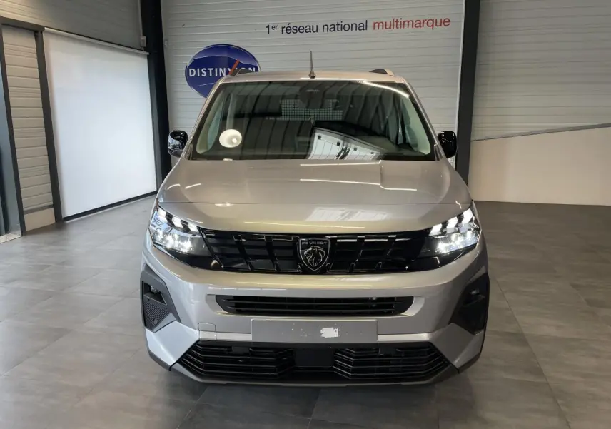 Vue avant du Peugeot Rifter gris Artense avec calandre noire et signature lumineuse LED allumée en intérieur showroom.