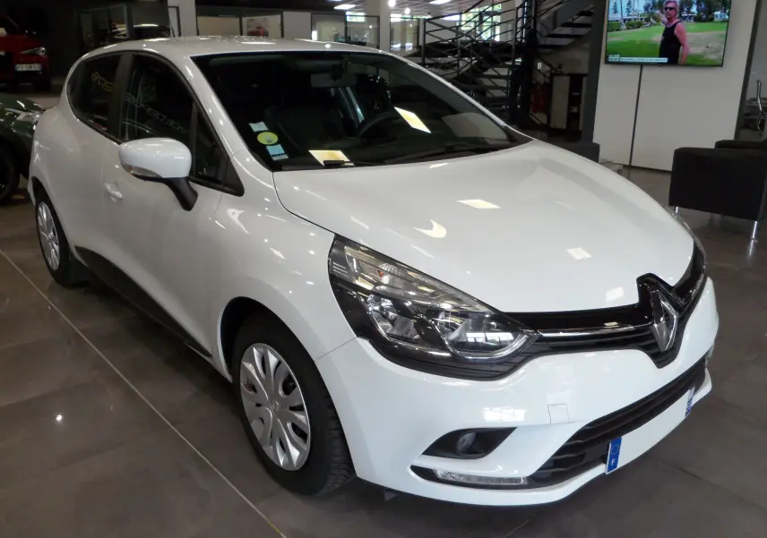 Renault Clio IV Société blanc Glacier vue 3/4 avant droit en intérieur avec jantes acier et phares allumés.