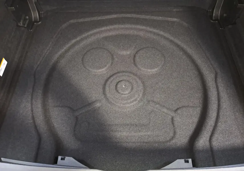 Coffre ouvert du Volkswagen Tiguan blanc pur 2025, vue plongeante sur l'espace de rangement sans roue de secours visible.