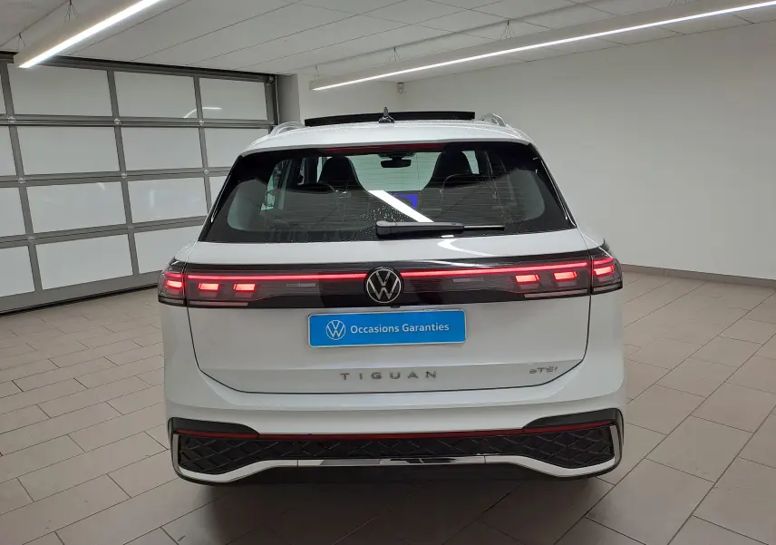 Vue arrière d'un Volkswagen Tiguan blanc pur 2025 avec feux LED allumés dans un garage lumineux.