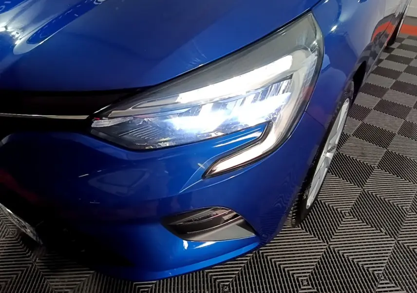 Gros plan sur l'avant droit de la Renault Clio Business bleu, mettant en valeur son phare LED allumé et la calandre.