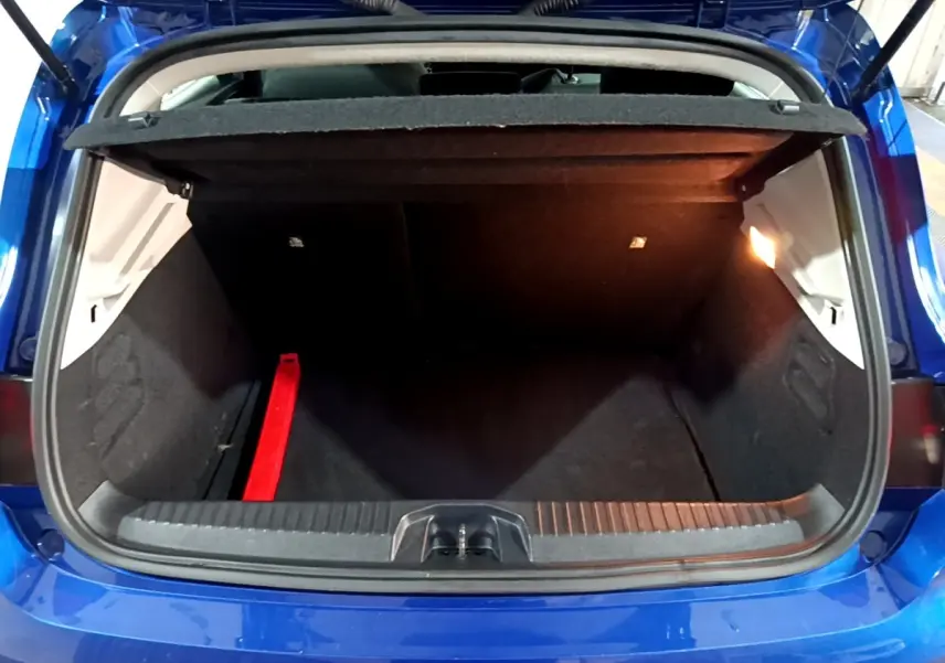 Coffre ouvert vu de l'arrière d'une Renault Clio Business bleu, avec tapis noir et lumière intérieure allumée.