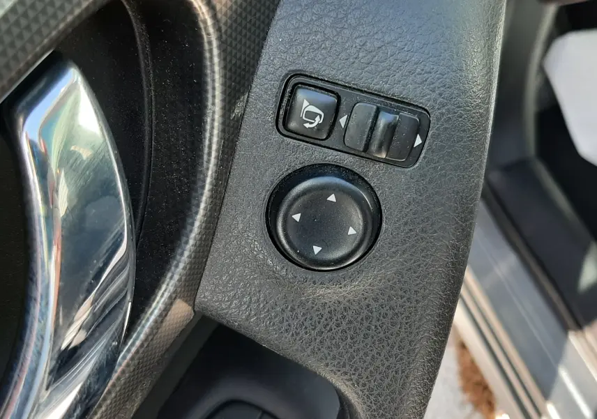 Gros plan sur les commandes de réglage des rétroviseurs et des vitres côté conducteur d’un Nissan Qashqai marron métal 2018.