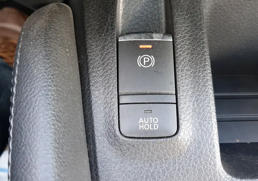 Gros plan sur les boutons de frein à main électronique et Auto Hold en plastique noir dans l'habitacle du Nissan Qashqai marron métal.