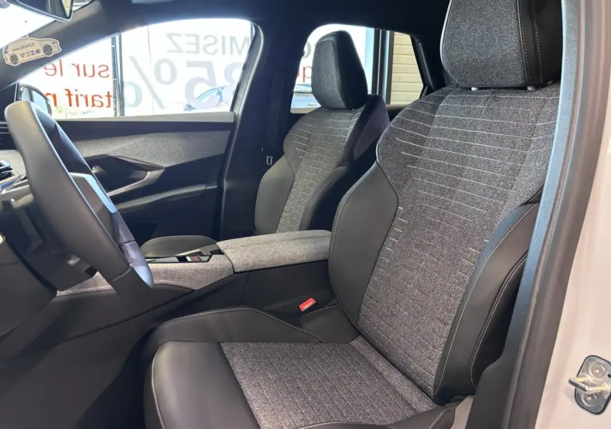 Vue intérieure côté conducteur du Peugeot 3008 blanc 2026, sièges tissu gris et cuir noir avec accoudoir central.