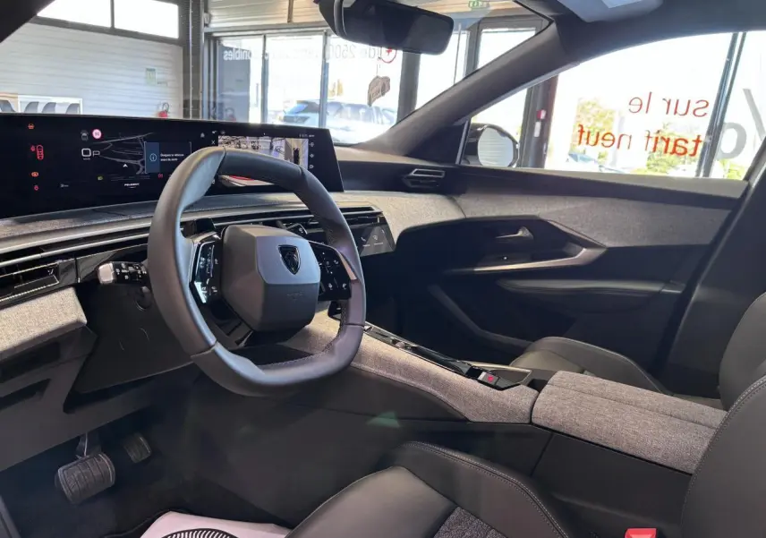 Vue intérieure côté conducteur du Peugeot 3008 Hybrid 2026, avec volant compact, tableau de bord numérique et habillage tissu gris chiné.