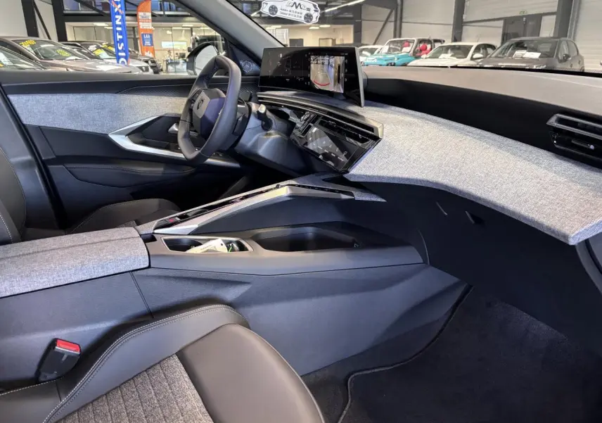 Vue intérieure côté conducteur du Peugeot 3008 Hybrid 2026, tableau de bord avec décor tissu gris et écran incurvé flottant.