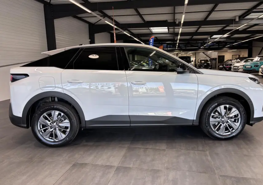 Profil droit d’un Peugeot 3008 blanc hybride 2026 en showroom avec jantes alliage 18 pouces et vitres teintées.