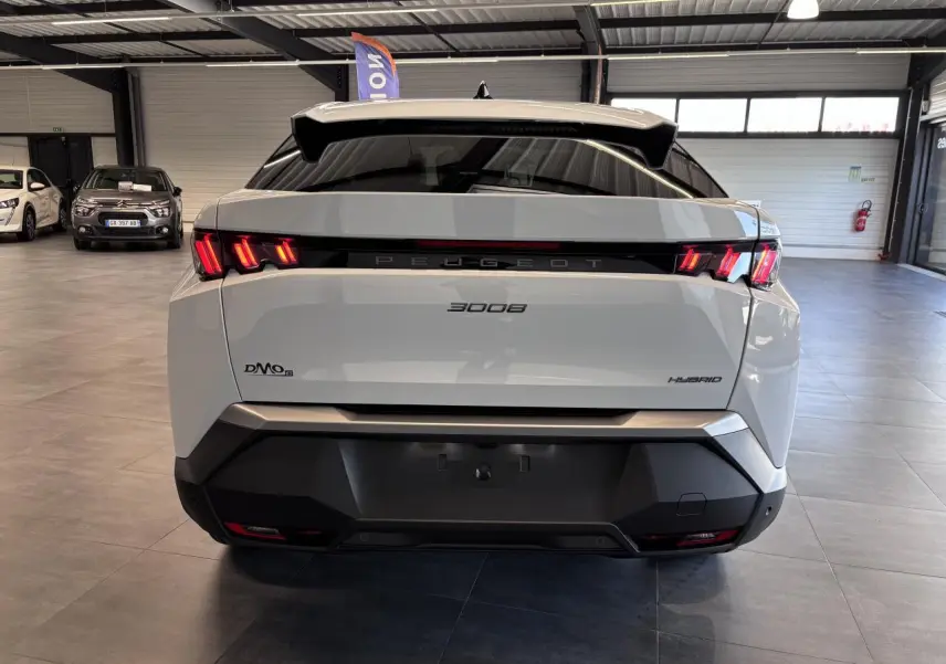 Vue arrière d'un Peugeot 3008 hybride blanc avec feux LED 3 griffes et bandeau noir laqué au showroom.
