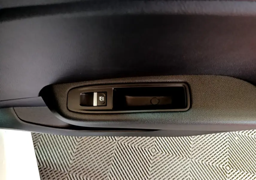 Détail de la commande de lève-vitre électrique sur la porte intérieure noire côté gauche d'une Renault Clio blanche.