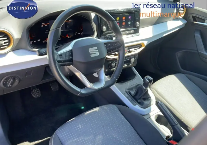 Vue intérieure de face du poste de conduite du SEAT Arona 2025, volant cuir noir, tableau de bord digital et levier de vitesse manuel.